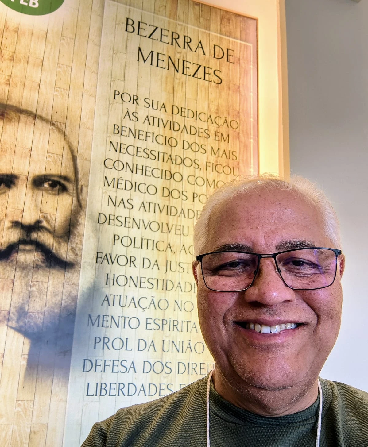Júlio Góes sorrindo, de óculos e camisa verde